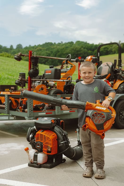 Tommy with a leaf blower in front of the equipment trailer